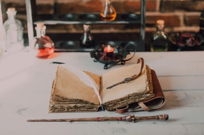 Раскрытая старинная книга фэнтези с пером, свечой и волшебной палочкой на столе