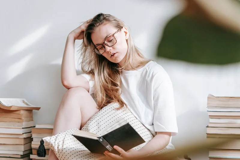 Девушка читает книгу среди стопок циклов Young Adult и романтического фэнтези